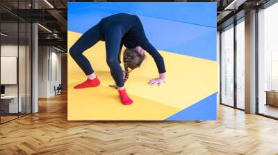 The child does gymnastics in the gym. Little girl doing bridge exercise on tatami mat. A sports child in a black tights bends in the back. Wall mural