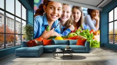 Group of young girls sitting next to each other in front of pile of vegetables. Wall mural