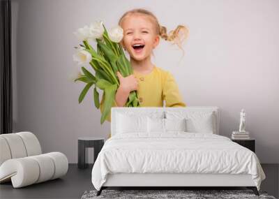 baby girl blonde with a bouquet of tulips on a light background.baby girl blonde smiling.spring and women's day concept.Cute little girl holding white tulips.copy spase Wall mural