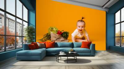 baby girl sitting with bag of vegetables on yellow isolate background, space for text. the concept of healthy eating.organic food Wall mural