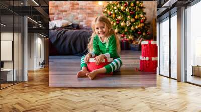 cute little girl in pajamas near the Christmas tree pulls out of the gift box kitten. Christmas gifts, simple strstnto for text Wall mural