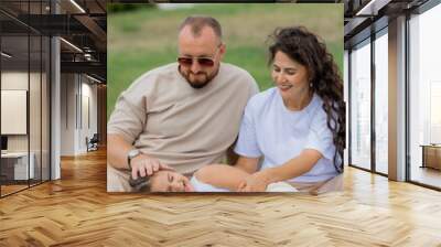 happy family is relaxing on a green lawn in the park in summer Wall mural