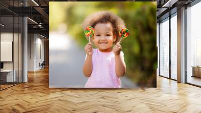 little African American girl in the summer on a walk smiling holding colorful candies Wall mural