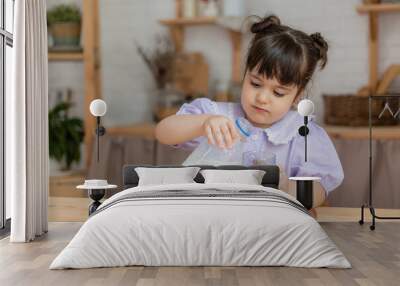 little girl in a lilac dress drinks milk and eats a bun at the kitchen table. space for text, banner Wall mural