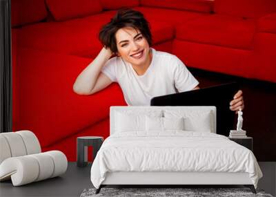 young brunette woman with short hair is smiling, working on a computer at home sitting on a red sofa. remote work. free schedule. distance learning Wall mural