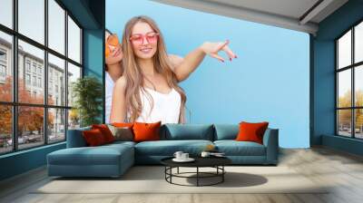 two young hipster woman friends in retro neon sunglasses standing and smiling over blue wall Wall mural