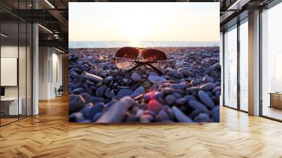 Sunglasses lie on a stone beach on the seashore Wall mural