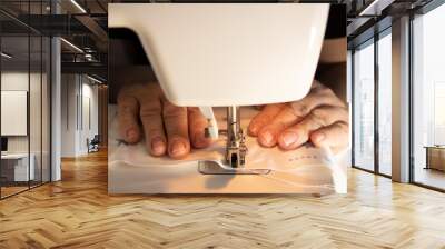 Close-up of an old senior successful professional, experienced designer, tailor, dressmaker, wrinkled hands working on a sewing machine Wall mural