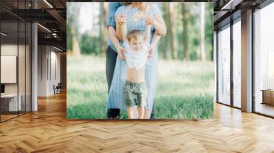 mother holding her son at a photo shoot to help him right pose for the photographer. Happy young family  outside in green nature Wall mural