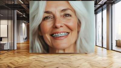 High-resolution close-up portrait of an elderly woman smiling, showcasing orthodontic gray metal braces on her teeth with beautiful white hair and clean background Wall mural