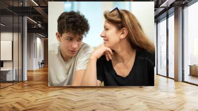 A middle-aged woman is good spending time with her son in a cafe, they sit and talk. Mom looks at her teenage son with love. Focus on mother Wall mural