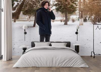 A teenage boy talking on the phone while walking in the park, the boy is warmly dressed because it is winter. The boy looks ahead anxiously, his father tells him something important by phone Wall mural