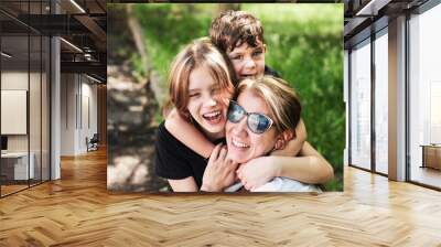 Happy mother surrounded by her children of different ages, a teenage daughter and a young son hugging their mother and having fun and talking together Wall mural