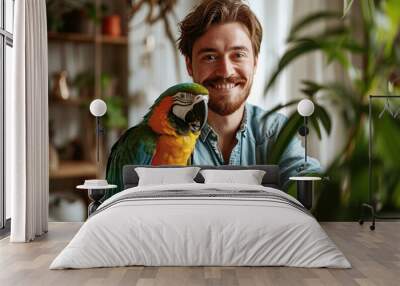 Beautiful orange blue green parrot and its owner a smiling handsome bearded young man in a room full of plants Wall mural