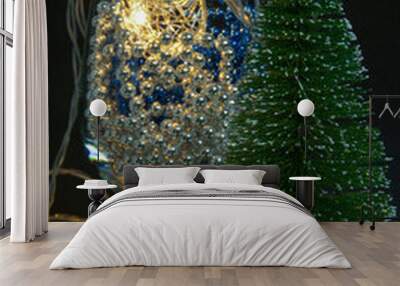 a wine glass on a black background stands next to a Christmas tree. the glass contains blue and silver Christmas decorations and a garland with beautiful yellow lights burning. Wall mural