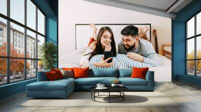 Man and woman in the bed look into smartphone, home isolation while quarantine Wall mural