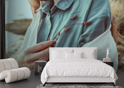 A close-up of woman's hand holding a wild flower. A young ginger woman standing by the lake shore in summertime. A red headed girl wearing i linen aquamarine blouse and linen white jacket. Wall mural