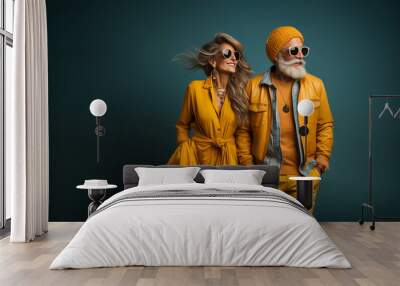 A modern stylish mature smiling couple, man and a woman in bright yellow fashionable clothes, black sunglasses and jewelry on a dark teal blue colored background Wall mural