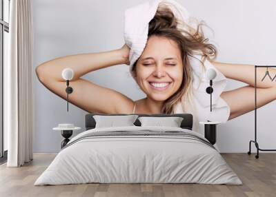 A young beautiful caucasian smiling woman dry her wet hair with a white towel on her head after a shower isolated on a white background. Hair care Wall mural