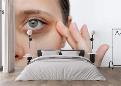 A young caucasian woman demonstrating dark circles under her eyes with hand isolated on a white background. Pale skin, bruises under the eyes are caused by fatigue, lack of sleep, insomnia and stress Wall mural