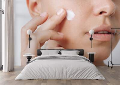 Close up of a young caucasian woman touching the face with her hand applying a smear of cream on the skin isolated on a white background. Nourishing moisturizing cream. Cosmetology and beauty Wall mural