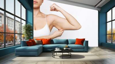 Cropped shot of a young caucasian slim woman grabbing skin on her upper arm with excess fat isolated on a white background. Pinching the loose and saggy muscles. Overweight, liposuction concept Wall mural