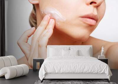 Cropped shot of a young caucasian woman touching the face with her hand applying a moisturizing cream on the skin isolated on a white background. Cosmetology and beauty concept Wall mural