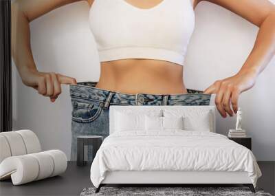 Cropped shot of a young slender woman dressed in wide jeans and white top demonstrates successful weight loss isolated on a white background. Diet and wellness concept Wall mural