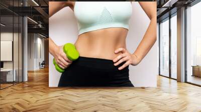 Cropped shot of a young slender woman with toned stomach with abs holding green dumbbells in her hand isolated on a white background. Result of fitness, diet, healthy lifestyle. Workout, exercises Wall mural