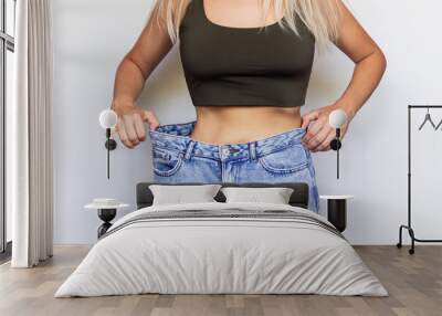 Cropped shot of a young slim woman dressed in wide jeans and short top demonstrates successful weight loss isolated on a light color gray background. Diet, wellness and health nutrition concept Wall mural