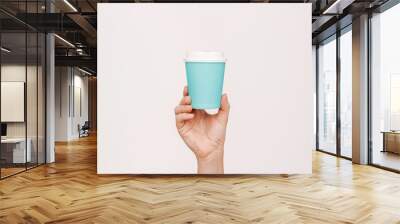 Woman's hand holding blue eco paper cup with white lid with tea or coffee isolated on light background. Mockup with empty copy space for text or design. Recycling eco-friendly concept. Blank for logo Wall mural