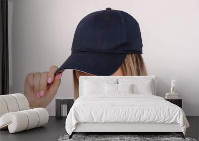 Young caucasian blonde woman holding the visor of the cap showing empty copy space for design or text on a white background Wall mural