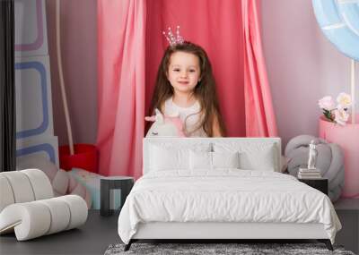 A little girl in a smart dress on the background of a beautiful children's room. Toy unicorn in his hands. Image of a little Princess in a crown Wall mural