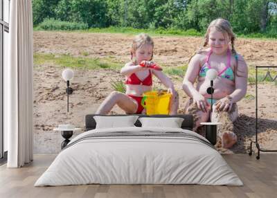 Girls play on the sandy beach by the lake in the summer heat.  Wall mural