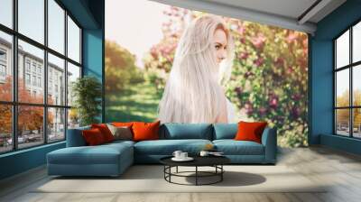 Woman with  long blond hair in the garden with flowers. Beautiful girl on a sunny day. Wall mural