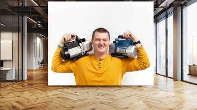 A strong man holds two vacuum pumps for refrigeration in his hands. Wall mural