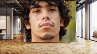 Close-up of a young Hispanic man with curly hair, looking confidently at the camera - Wall mural