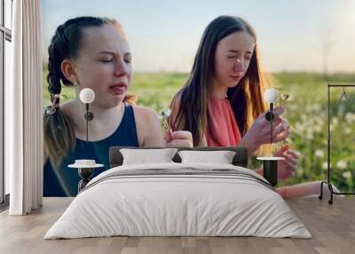 two teenage sisters in summer dresses blowing dandelions in meadow Wall mural