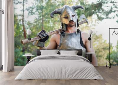 Portrait of a warrior in a horned helmet, a steel breastplate with a two-handed ax in his hands, posing against the backdrop of the forest.  Wall mural