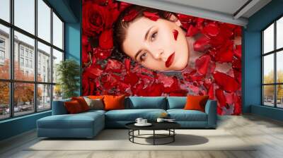 Top view, close-up face of a young woman in a bathtub full of red rose petals. Beauty portrait of an attractive girl. Spa treatment for skin rejuvenation. Wall mural