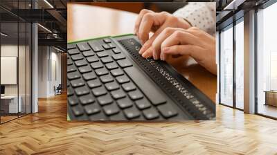 a blind woman uses a computer with a braille display and a computer keyboard. inclusive device. Wall mural