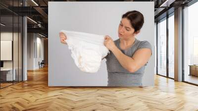 A caucasian woman holds an adult diaper and checks its strength on a white background.  Wall mural