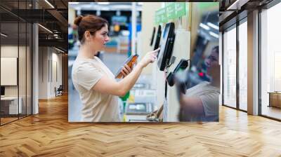 A frustrated woman uses a self-checkout counter. The girl does not understand how to independently buy groceries in the supermarket without a seller Wall mural