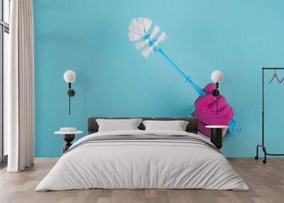 A woman's hand in a rubber glove holds a toilet brush and sticks out of a hole on a blue paper background. Wall mural