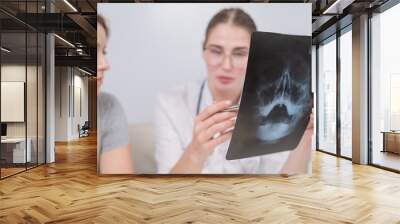 A woman doctor and a patient at the reception are discussing an x-ray of the sinuses. Wall mural