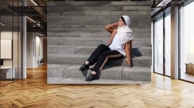 A young woman dressed in a hijab and a business suit is sitting on the stairs.  Wall mural