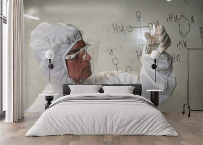 An elderly Caucasian male chemist in a protective suit looks at a test tube against the background of a glass wall with formulas.  Wall mural