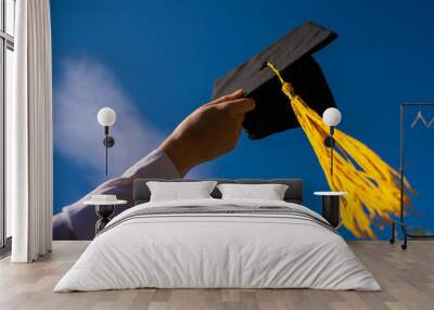 Close-up of a woman's hand with a graduation cap against the blue sky.  Wall mural