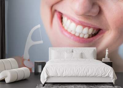 Close-up portrait of a beautiful caucasian woman with a flawless smile holding a toothpick with dental floss on a white background Wall mural