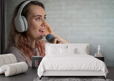 Close-up portrait of a caucasian woman with curly hair singing into a microphone. Beautiful sensual girl in white headphones sings a song in home karaoke. Wall mural